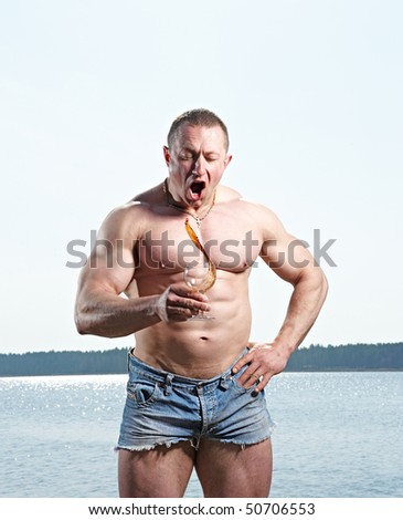 Muscular man with glass of red drink at  lake on sunny day splashing drink