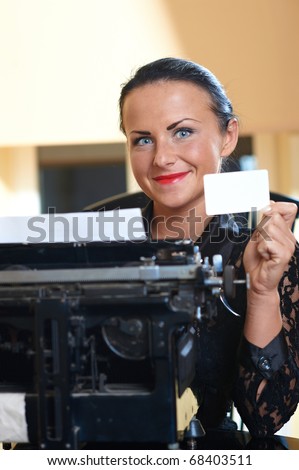 Young pretty woman sitting at a typewriter with white blank card in hand