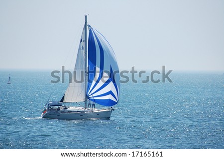 A fully crewed racing yacht with a blue and white spinnaker catching the wind