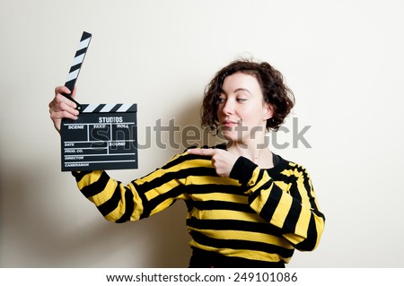 Girl in yellow t-shirt with smiling face pointing out a movie clapper on white background