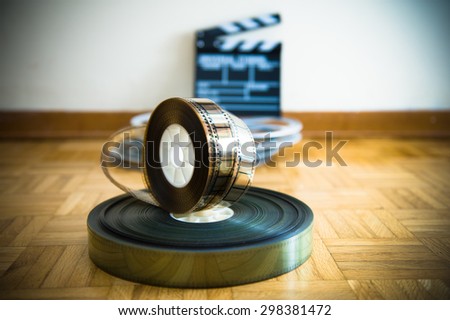 35 mm cinema film reel and out of focus movie clapper board in background on wooden floor