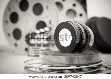 Heap of old 35 mm movie reels with out of focus clapper and boxes in background, vintage black and white