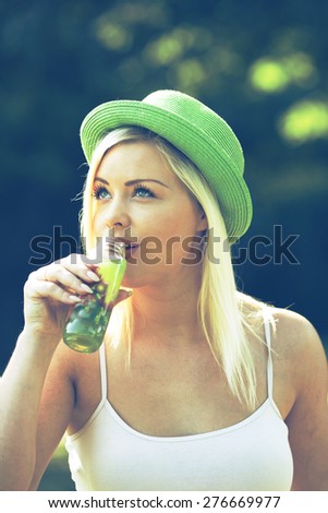 20-25 years woman drinking green juice outdoor in park at summertime