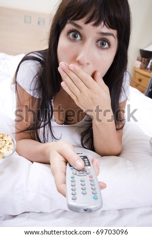 attractive young woman watching a scary and horror movie in tv alone in a room
