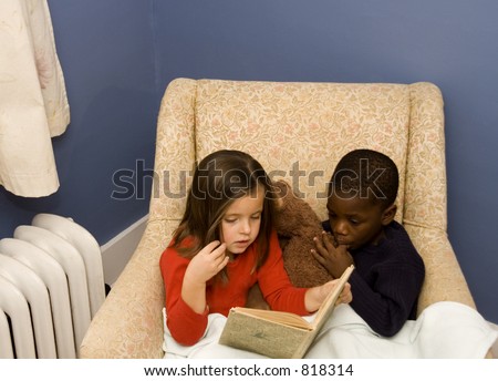 Two small children reading together in a big chair.  Diversity.