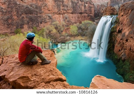 Woman sitting at the edge of a cliff watching Havasu Falls drop into it's turquoise pool. Havasu Canyon, Arizona. Havsupai Reservation.