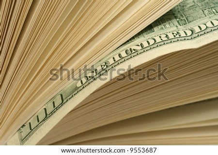 Close-up of one hundred dollars bill between pages of book. Pages of book looking as a stack of bills