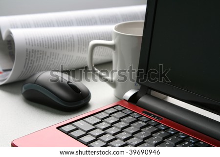 The close-up of red laptop, white cup, computer mouse and newspaper