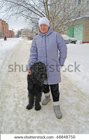 The woman costs in the street in winter clothes with a dog, Russian Black Terrier, winter in Moscow Region, Russia
