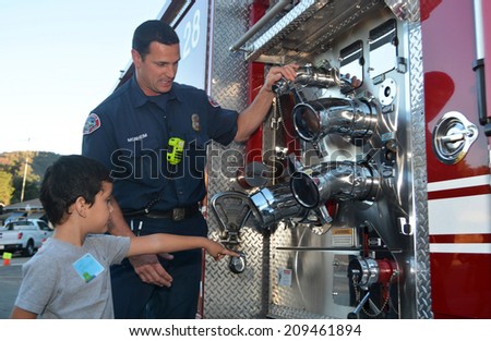 GLENDALE, CA - AUGUST 5, 2014: A firefighter explains his job to young boy pointing at his fire truck as part of a National Night Out against crime community fair.