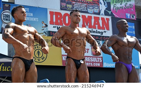 VENICE, CA SEPTEMBER 1, 2014:  Three bodybuilders stand in a line posing and flexing muscles at the Muscle Beach Championship bodybuilding competition on September 1, 2014 at Venice Beach, CA.