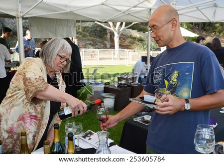 LA CRESCENTA, CA - SEPTEMBER 28, 2014: A woman leans over a table pouring red wine for a man holding a glass during a public wine tasting event in La Crescenta, CA on September 28, 2014.