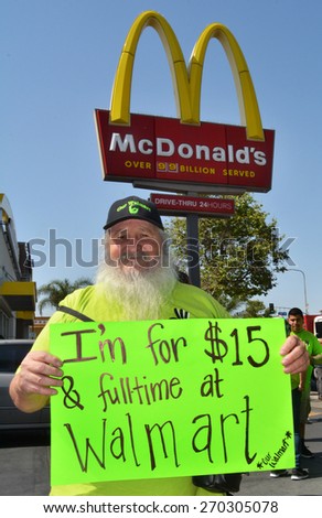 LOS ANGELES, CA   APRIL 15, 2015: A protestor stands near a McDonald\'s sign, holding a sign advocating raising the minimum wage at Walmart during a demonstration in Los Angeles on April 15, 2015.