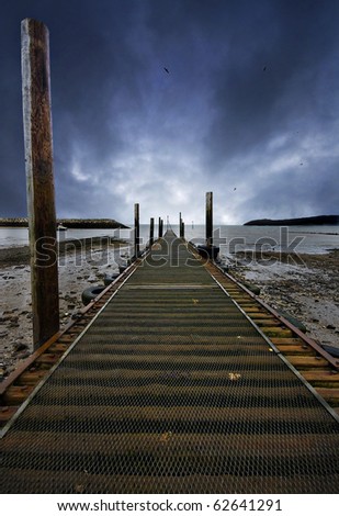 fishing jetty at low tide with vanishing point at the bright part of a threatening sky