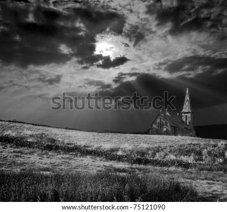 dramatic and moody black and white image of a church on a hill being lit by sunbeams after a storm