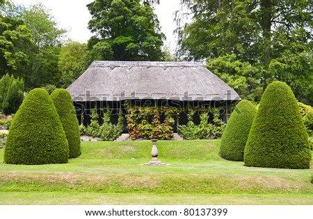 an old but restored summer house with traditional reed thatched roof in a formal garden setting