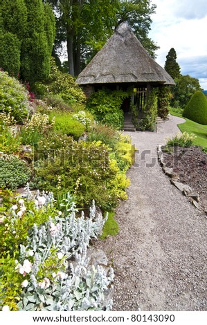 a gravel path leads through beautiful flower beds to a restored victorian summer house with traditional reed thatched roof.