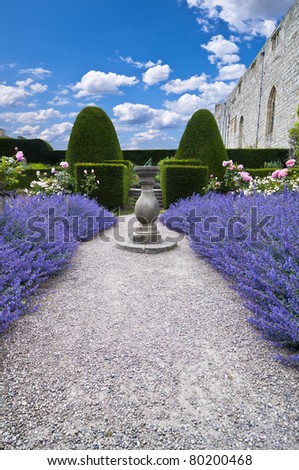 wide angle view of a gravel pathway leading through lavender beds to an old stone sundial and formal trimmed hedges behind