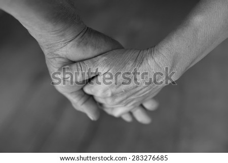 Hand of an elderly woman holding the hand of an elderly man. black and white.