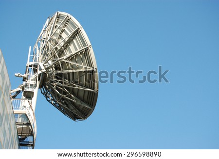 A large, industrial satellite dish used in the communications industry against a blue sky on a sunny, summer day with space for copy.