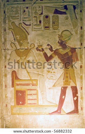 An ancient Egyptian painted hieroglyphic carving of the Pharaoh Seti making a religious offering to the god of the underworld - Osiris.  Niche at the Temple to Osiris at Abydos, Egypt.