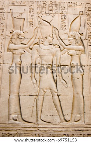 Ancient Egyptian hieroglyphic carving of the Pharaoh king of Egypt with the goddesses Isis and Maat either side of him.  Outer wall of the Temple of Horus, Edfu, Egypt.