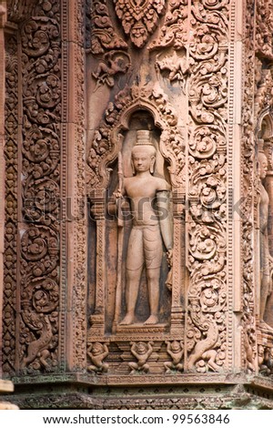 A guardian sculpture on the outer wall of a prasat, or chapel, at Banteay Srei Temple, Angkor, Cambodia.  Intricate Khmer carving in red sandstone over 1000 years old.