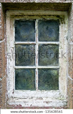 An old weathered window frame, in portrait, moss and cobwebs line the glass panes and the paint is peeling off