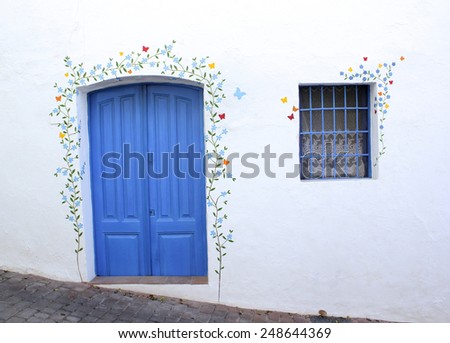 A blue door and window in a wall with a mural on a steep cobbled street