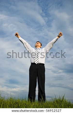 A young businessman is staying outdoors in victory pose on a very cloudy background