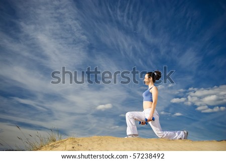 young woman squats with dumbbells on the sand