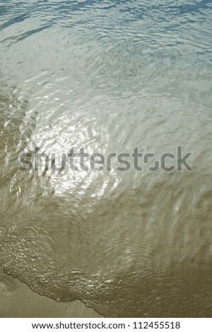 Shallow ocean water over sandy beach with sunshine reflecting in water