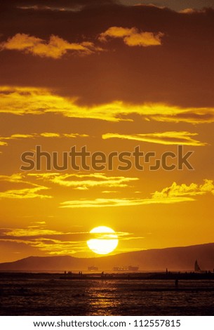 Sun in dramatic sky above dryland and ocean in sunset