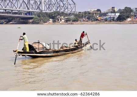 KOLKATA, INDIA - OCTOBER 27: Old wooden boat crosses the Hooghly River nearby the Howrah Bridge on October 27, 2009.  To use a small wooden ferry is a cheap way how to cross the Hooghly River.