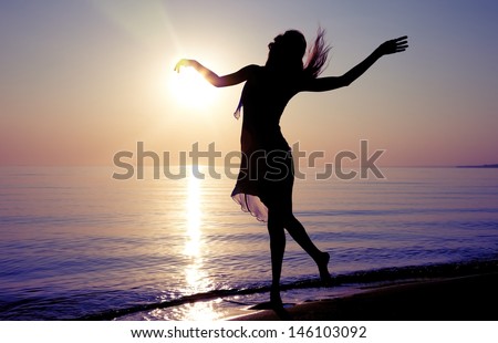 Silhouette of the woman dancing at the beach during beautiful sunrise. Natural light and darkness