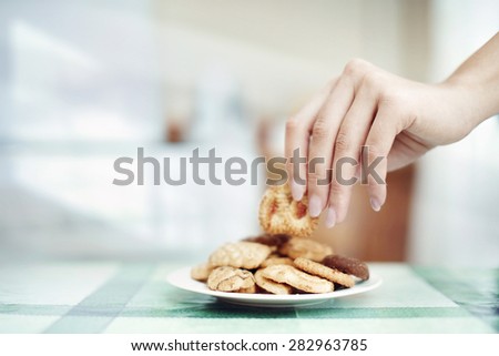 Human hand taking cookie in plate on a table