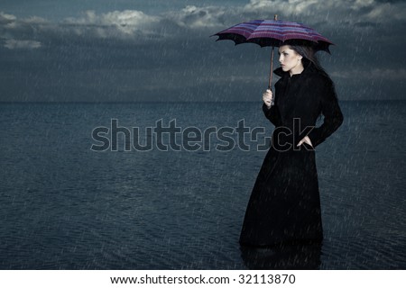 Lady with umbrella standing under the rain in the sea