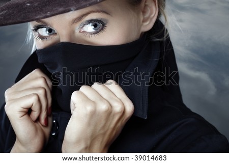 Female spy in hat with face covered by the coat collar