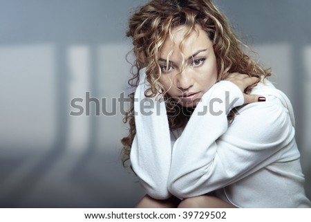 Sad Latin lady with curly hairs sitting indoors. Horizontal photo