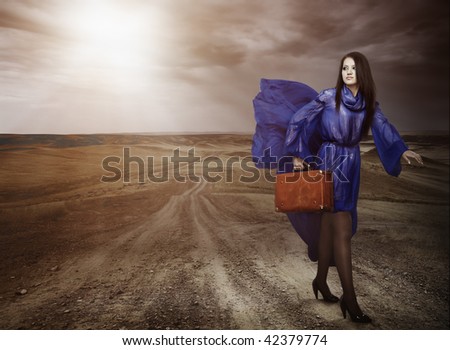 Elegant young lady in the blue stylish dress carrying the bag and going by the byroad