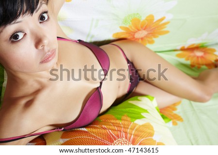 Asian brunette lady in  lingerie laying on the bed with colorful linen