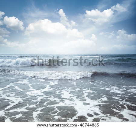 View on the blue sea with waves and spindrift under the cloudy sky