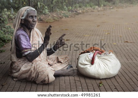 Horizontal photo of the poor old woman sitting outdoors near her things