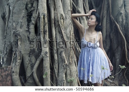 Alone sad brunette in the jungle standing near the huge old banyan tree. Grain and gauze added