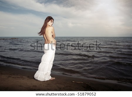 Topless lady with long hairs standing near the cold sea. Horizontal photo