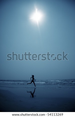 Woman at the beach running to the water in the deep dark night. Blue color toning added for coolness of the night