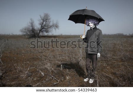 Sad alone clown outdoors holding umbrella and waiting for the rain. Artistic darkness and colors added