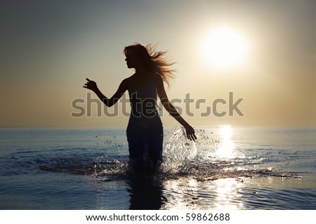 Silhouette of the woman with long hairs walking in the water during sunrise. Natural darkness and colors