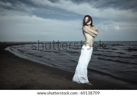 Single topless lady in the white shirt standing near the sea. Hairs are blown by the wind. Artistic colors and darkness added