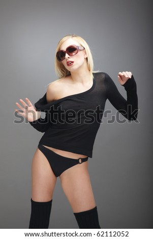 Blond lady in black stylish lingerie and fashionable sunglasses posing in the studio on a dark gray background